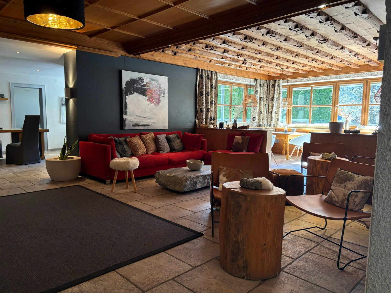 Wohnzimmer mit rotem Sofa, Fellteppich, Holzdecke und Panoramafenster – MONTAFONLodge