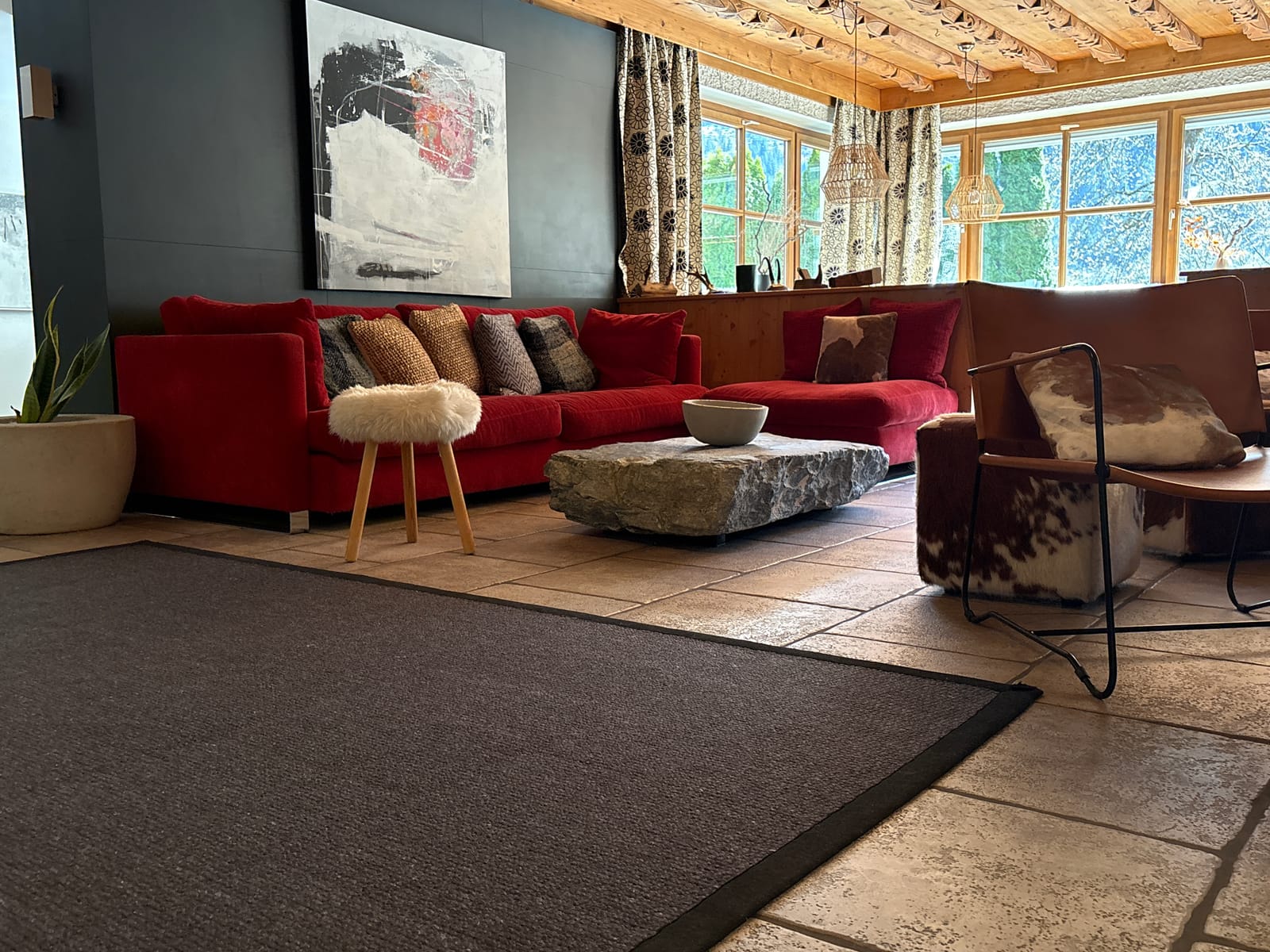 Rotes Sofa mit Fell-Hocker und Steintisch auf Teppich – MONTAFONLodge