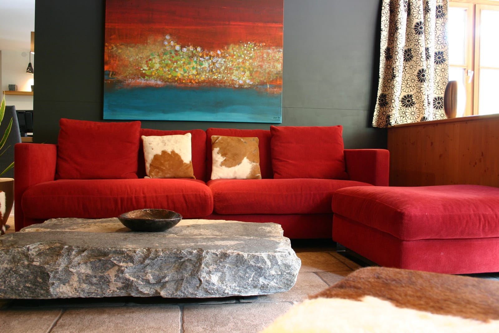 Rotes Ecksofa mit Kissen, Wandbild und Steintisch – MONTAFONLodge