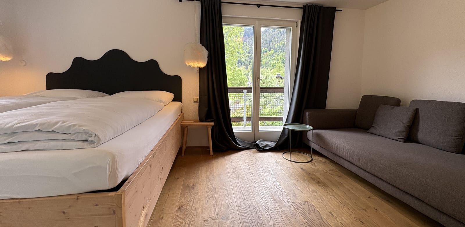 Schlafzimmer mit Bett am Fenster, Vorhänge und Sofa – MONTAFONLodge