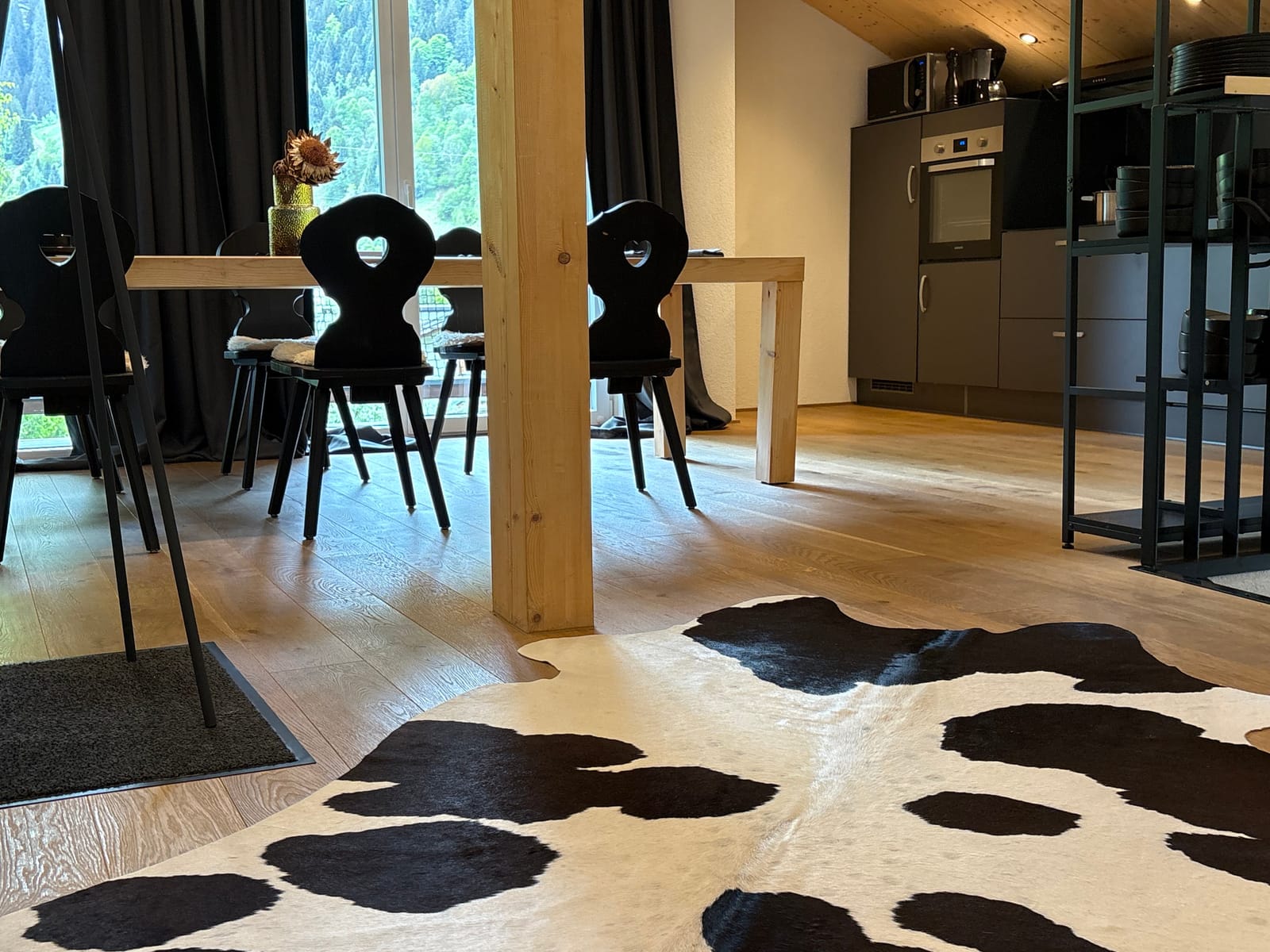 Essbereich mit Holztisch, schwarzen Stühlen, Kuhfell-Teppich und offener Küche – MONTAFONLodge