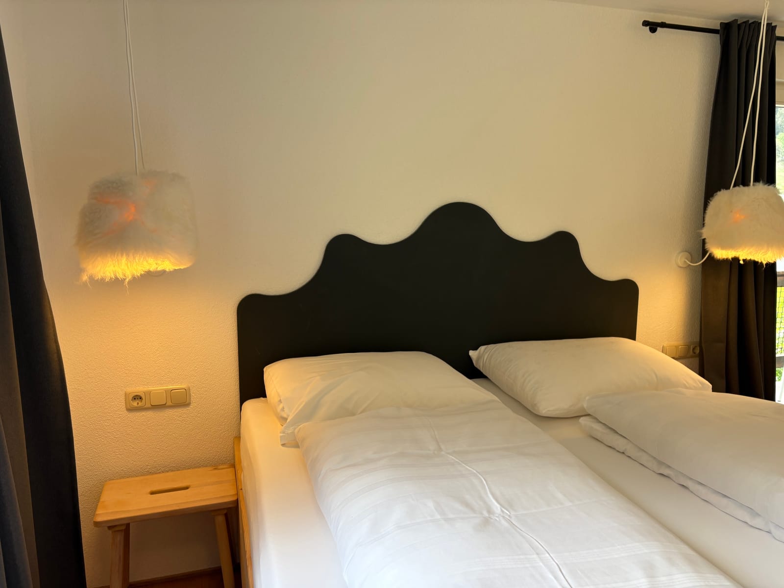 Doppelbett mit geschwungenem dunklem Kopfteil und Wandleuchten – MONTAFONLodge