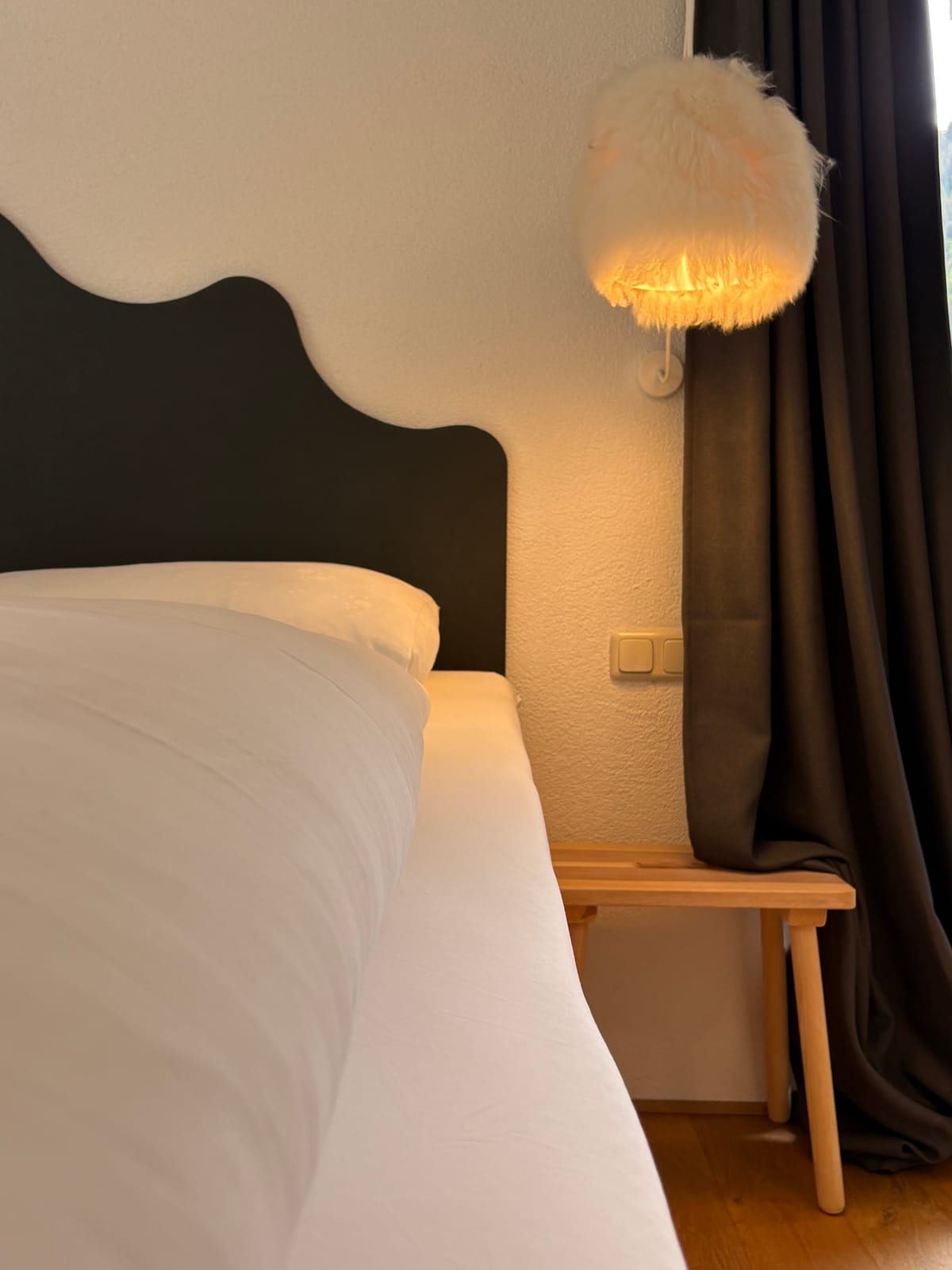 Bett mit geschwungenem dunklem Kopfteil und Wandleuchte – MONTAFONLodge