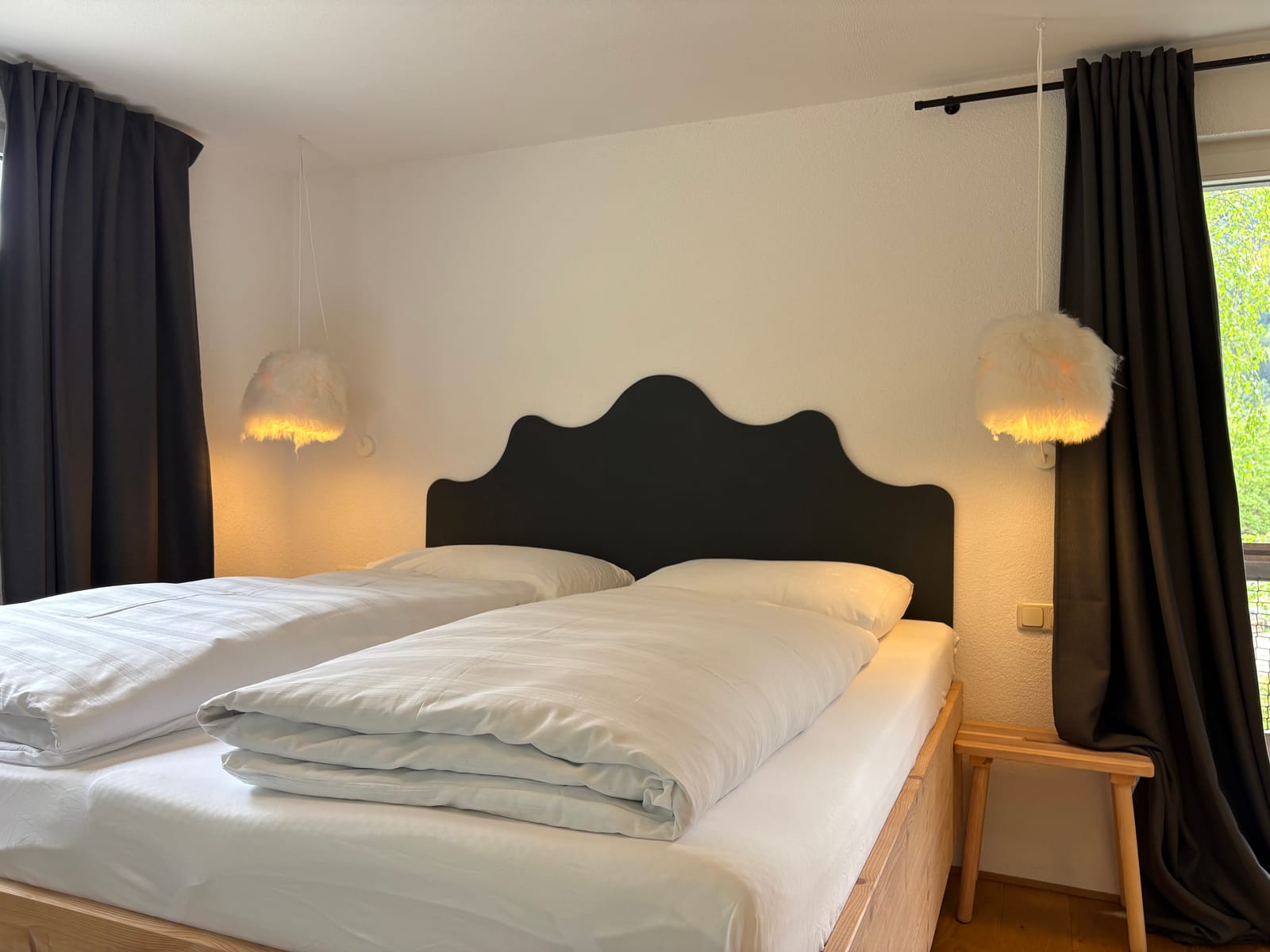 Doppelbett mit dunklem geschwungenem Kopfteil und Nachttischen – MONTAFONLodge