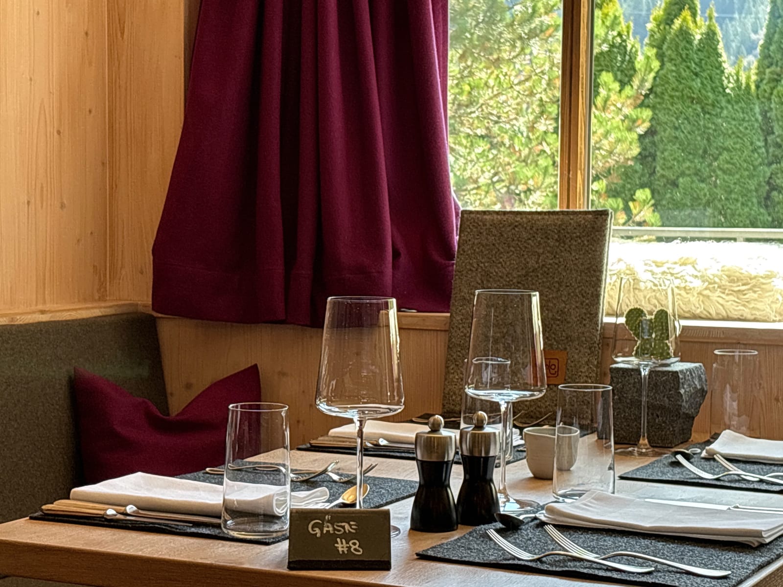 Gedeckter Tisch am Fenster mit Weingläsern und roten Vorhängen – MONTAFONLodge