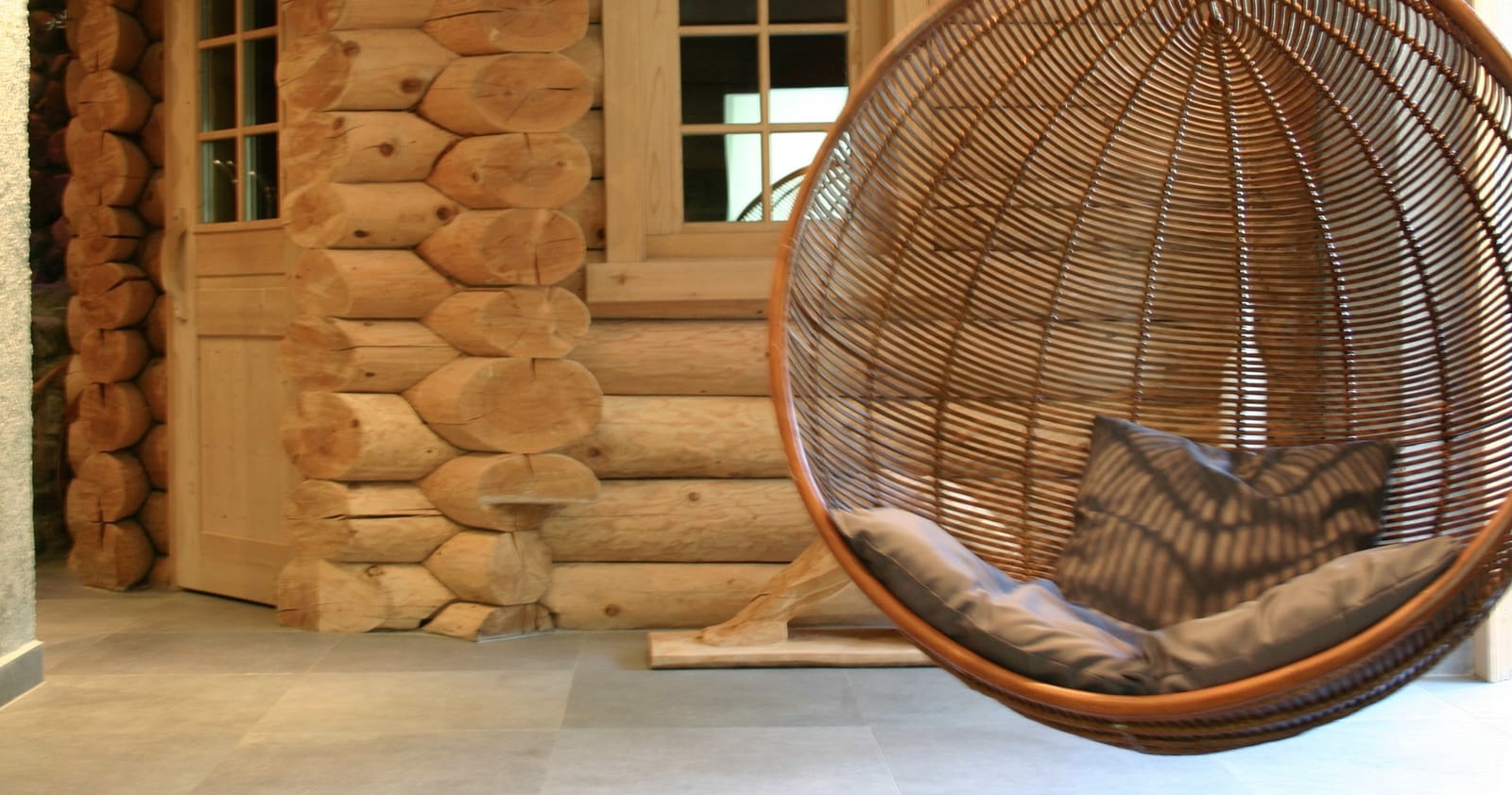 Rattan-Hängesessel vor Blockhauswand – MONTAFONLodge