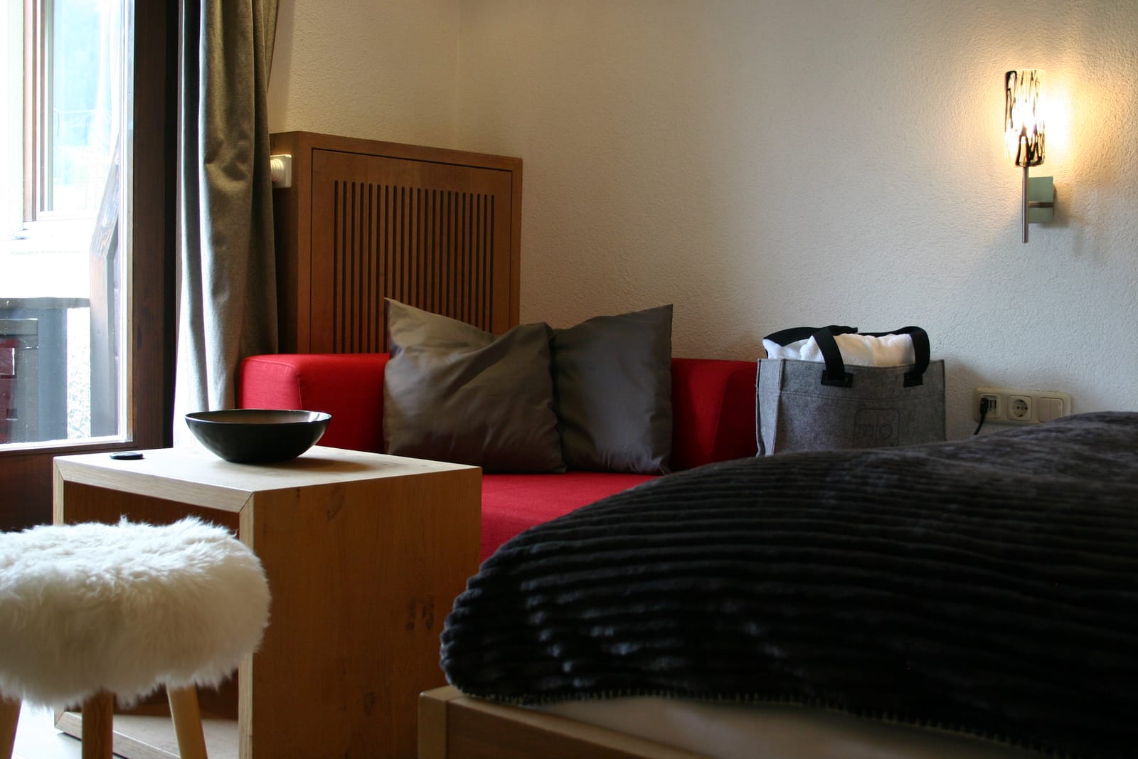 Doppelbett mit rotem Sofa, Beistelltisch mit Deko-Schale und Schaffell-Hocker – MONTAFONLodge