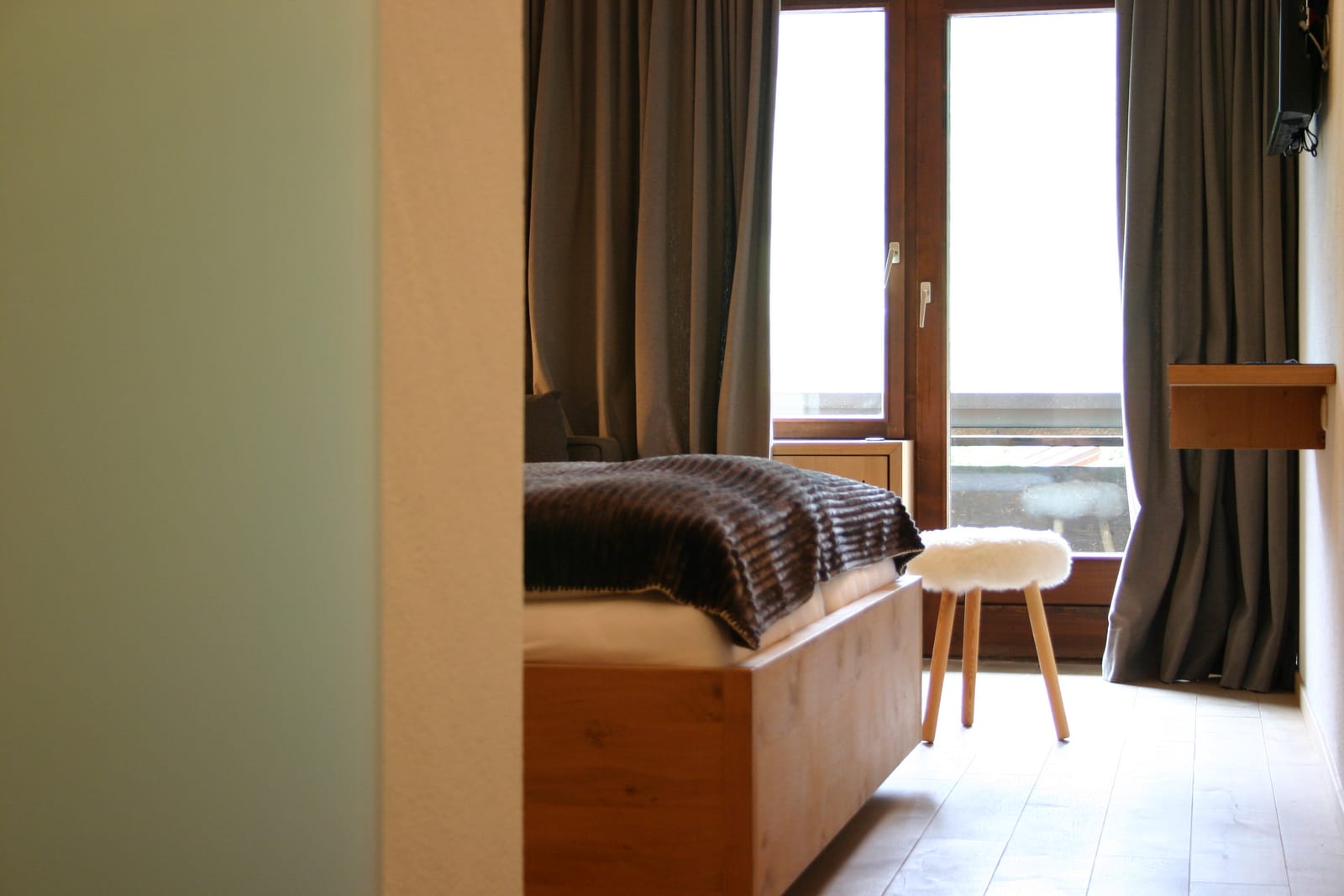 Bett am Fenster mit Balkontür, Hocker und Vorhängen – MONTAFONLodge