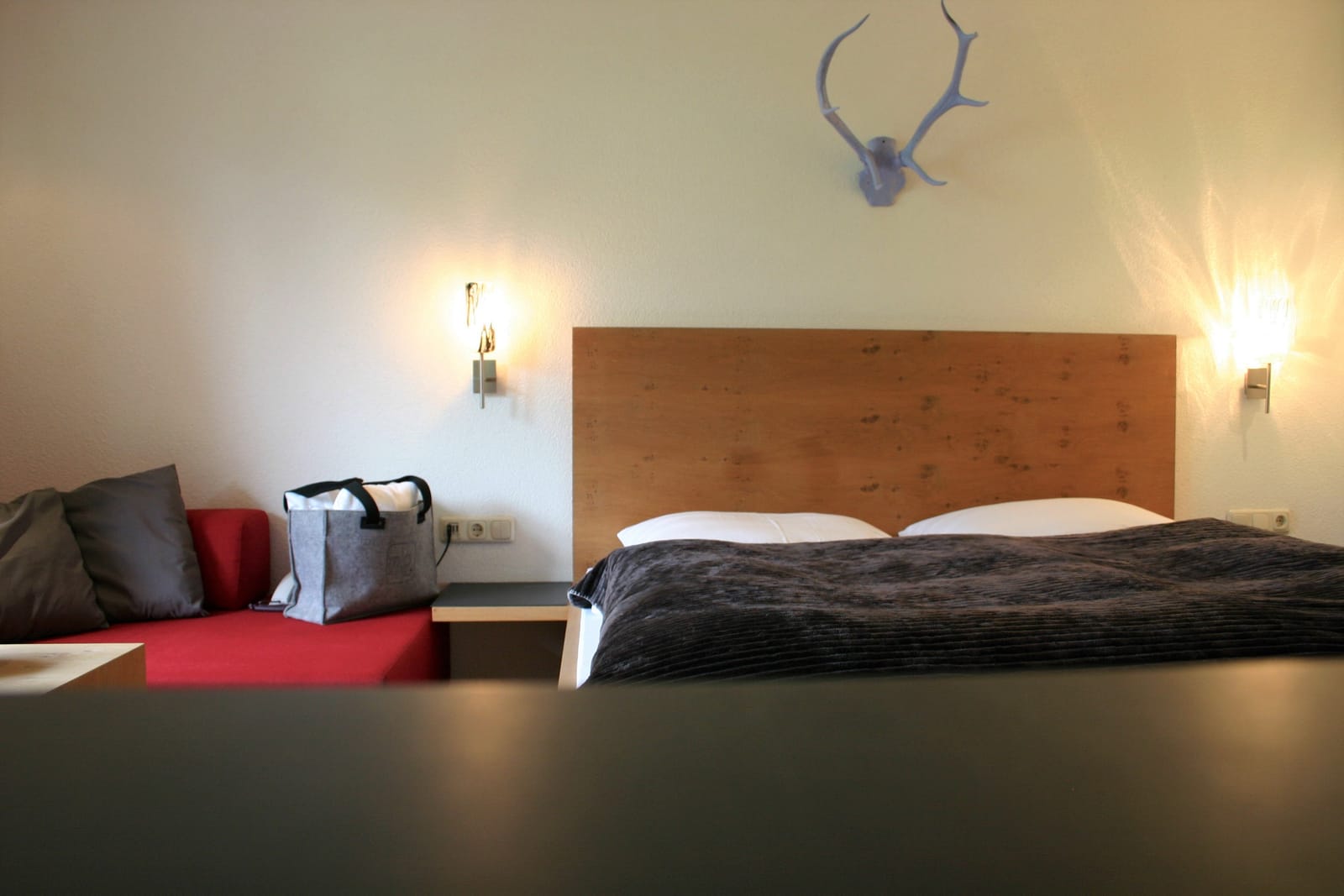 Doppelbett mit rotem Sofa seitlich, Geweih-Deko und Wandleuchten – MONTAFONLodge