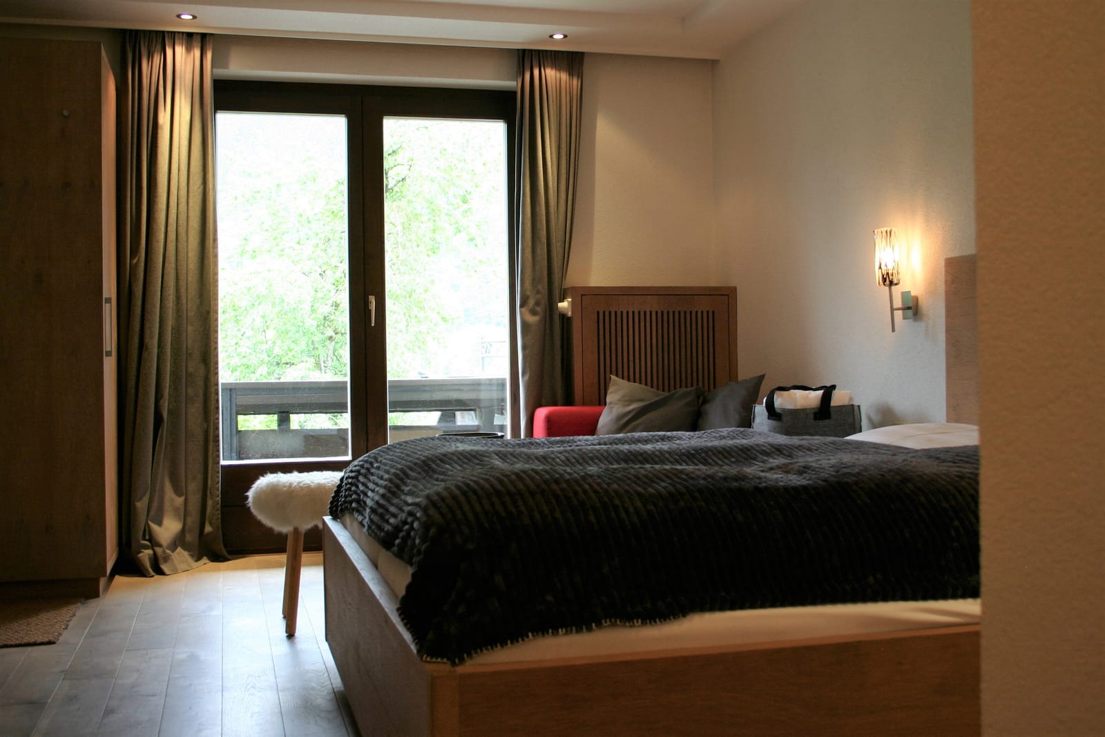 Doppelzimmer mit Balkontür und Vorhängen, Hocker am Bettende – MONTAFONLodge