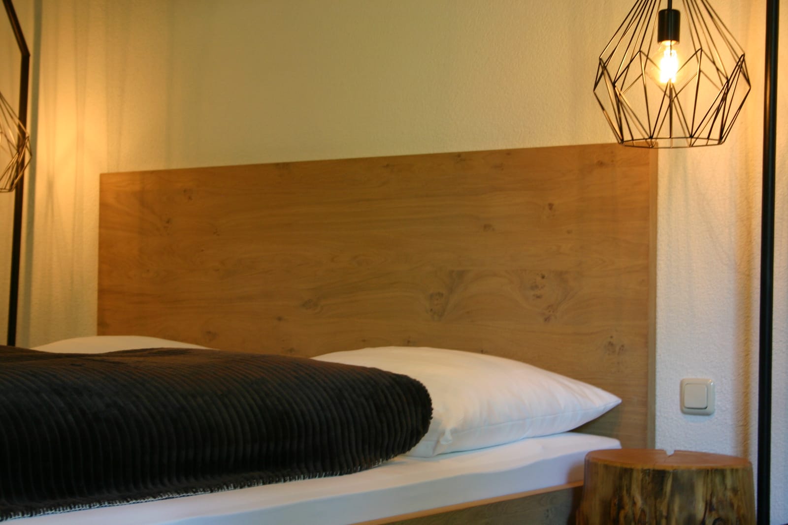 Bett mit Zirben-Kopfteil, Pendelleuchte und Baumstamm-Hocker – MONTAFONLodge