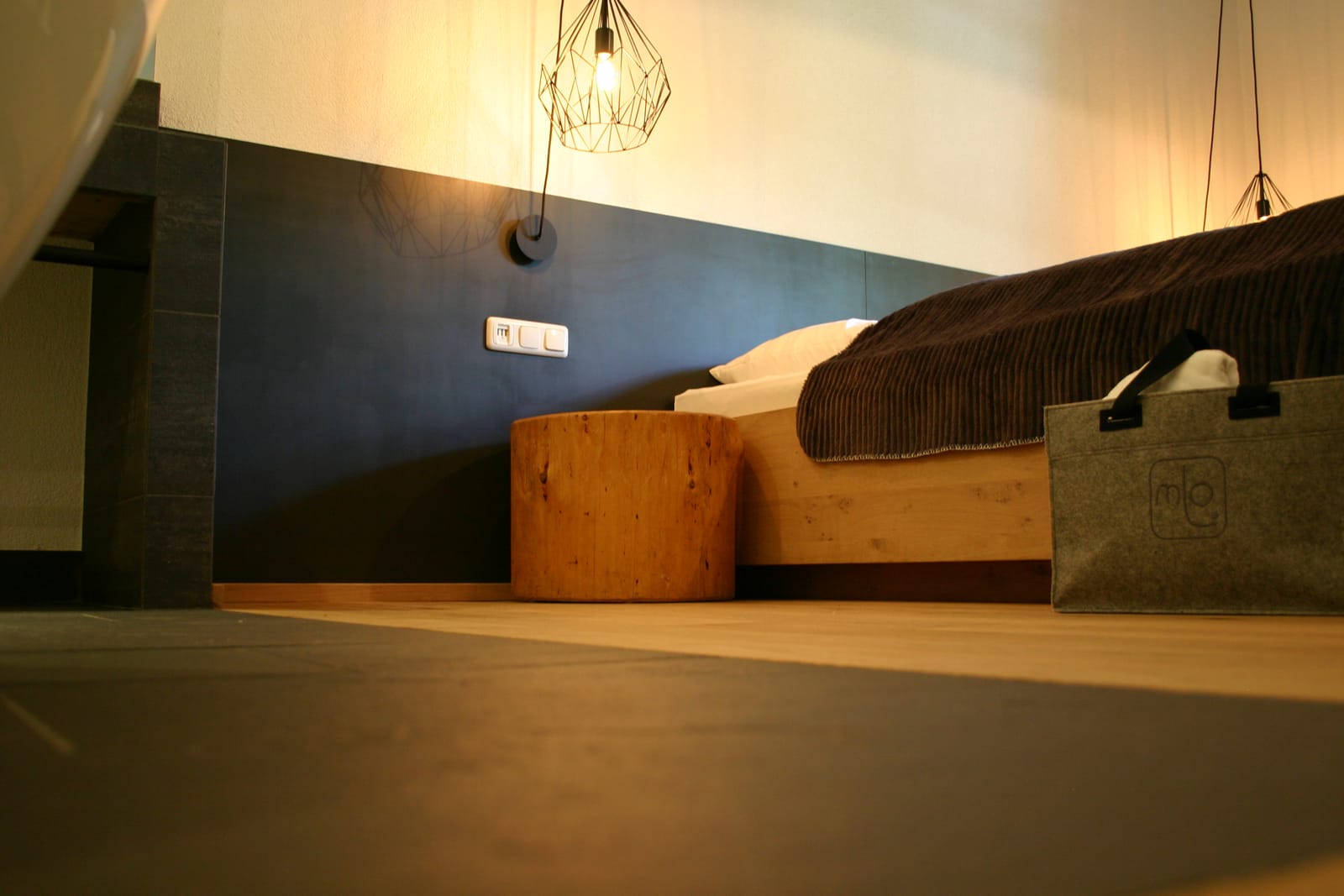 Doppelbett auf Podest vor dunkler Wand, Deko-Tasche – MONTAFONLodge